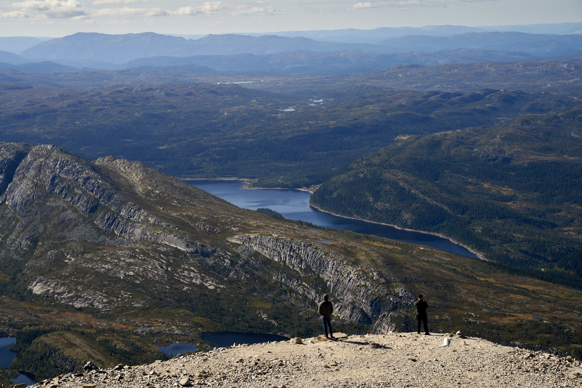 Two hikers on a summit looking out over a valley dotted with lakes